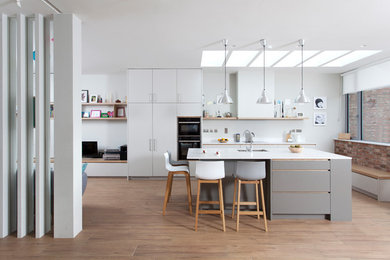 Mid-sized contemporary single-wall open plan kitchen in Dublin with flat-panel cabinets, white splashback, black appliances, laminate floors, with island, an undermount sink, white cabinets and brown floor.