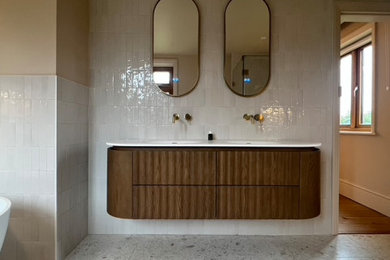 Design ideas for a large contemporary ensuite half tiled bathroom in Sussex with dark wood cabinets, a freestanding bath, a built-in shower, a one-piece toilet, white tiles, porcelain tiles, pink walls, terrazzo flooring, a wall-mounted sink, engineered stone worktops, multi-coloured floors, a hinged door, white worktops, a wall niche, double sinks and a floating vanity unit.