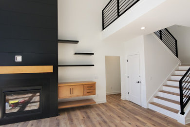 Источник вдохновения для домашнего уюта: огромная открытая гостиная комната в стиле модернизм с белыми стенами, полом из ламината, стандартным камином, фасадом камина из дерева и бежевым полом