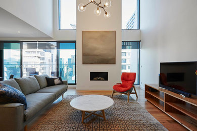 Photo of a small contemporary formal loft-style living room in Melbourne with white walls, medium hardwood floors, a plaster fireplace surround and a freestanding tv.
