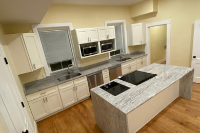 Eat-in kitchen - large eat-in kitchen idea in Boston with an undermount sink, shaker cabinets, beige cabinets, granite countertops, gray backsplash, granite backsplash, stainless steel appliances, an island and gray countertops