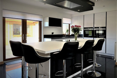 Design ideas for a medium sized modern l-shaped kitchen/diner in Other with a submerged sink, flat-panel cabinets, white cabinets, black appliances, an island, black floors and white worktops.
