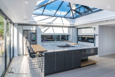 Photo of a large l-shaped kitchen/diner in Sussex with an integrated sink, flat-panel cabinets, white cabinets, quartz worktops, glass sheet splashback, black appliances, an island and white worktops.