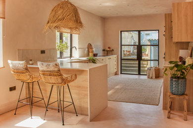 Large tuscan l-shaped concrete floor and pink floor eat-in kitchen photo in Cornwall with an undermount sink, flat-panel cabinets, light wood cabinets, solid surface countertops, beige backsplash, ceramic backsplash, black appliances, a peninsula and beige countertops
