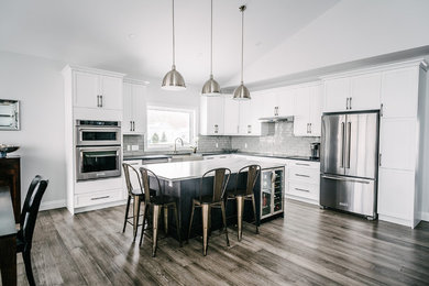 This is an example of a large transitional l-shaped eat-in kitchen in Other with a farmhouse sink, shaker cabinets, white cabinets, quartz benchtops, grey splashback, glass tile splashback, stainless steel appliances, medium hardwood floors, with island and brown floor.
