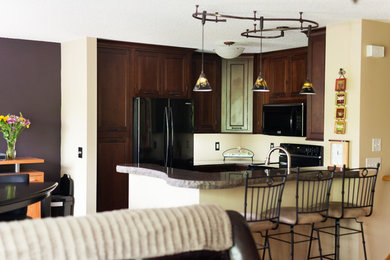 Inspiration for an u-shaped medium tone wood floor eat-in kitchen remodel in Minneapolis with an undermount sink, beaded inset cabinets, dark wood cabinets, granite countertops, black appliances and a peninsula