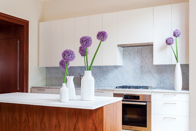 Inspiration for a mid-sized scandinavian galley medium tone wood floor eat-in kitchen remodel in Boston with an undermount sink, flat-panel cabinets, white cabinets, marble countertops, stainless steel appliances, an island, gray backsplash and stone slab backsplash