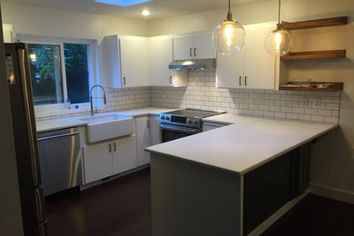 Small trendy u-shaped eat-in kitchen photo in Portland with a farmhouse sink, flat-panel cabinets, white cabinets, solid surface countertops, white backsplash, subway tile backsplash, stainless steel appliances and a peninsula