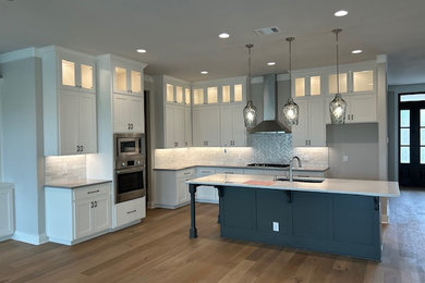 Kitchen - country laminate floor and brown floor kitchen idea in Austin with an undermount sink, shaker cabinets, white cabinets, quartzite countertops, beige backsplash, subway tile backsplash, stainless steel appliances, an island and white countertops