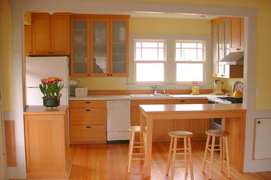 Example of a mid-sized classic u-shaped light wood floor eat-in kitchen design in Seattle with a double-bowl sink, shaker cabinets, light wood cabinets, solid surface countertops, yellow backsplash, white appliances and a peninsula