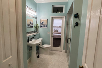 Mid-sized beach style 3/4 multicolored tile and porcelain tile porcelain tile, beige floor and single-sink bathroom photo in Orlando with flat-panel cabinets, white cabinets, a two-piece toilet, blue walls, a pedestal sink, quartz countertops, a hinged shower door, white countertops and a built-in vanity