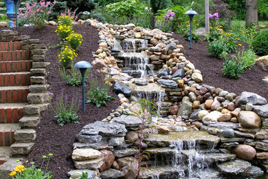This is an example of a country backyard garden in Cincinnati with a water feature and natural stone pavers.