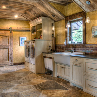 ミネアポリスの大きいラスティックスタイルのおしゃれな洗濯室 (ダブルシンク、インセット扉のキャビネット、白いキャビネット、御影石カウンター、黄色い壁、スレートの床、左右配置の洗濯機・乾燥機、マルチカラーの床、黒いキッチンカウンター) の写真