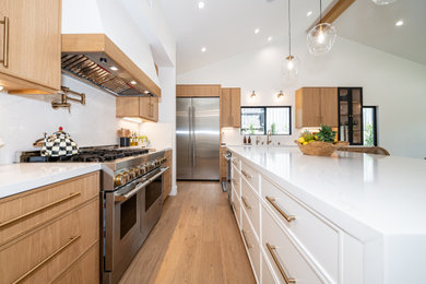 Eat-in kitchen - large medium tone wood floor, brown floor and vaulted ceiling eat-in kitchen idea in Los Angeles with an undermount sink, flat-panel cabinets, light wood cabinets, quartz countertops, white backsplash, quartz backsplash, stainless steel appliances, an island and white countertops