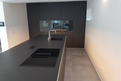 Offene, Zweizeilige, Große Moderne Küche mit integriertem Waschbecken, flächenbündigen Schrankfronten, schwarzen Schränken, schwarzen Elektrogeräten, Kücheninsel und schwarzer Arbeitsplatte in Dortmund