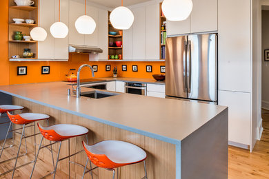 Example of a trendy u-shaped light wood floor kitchen design in Philadelphia with an undermount sink, flat-panel cabinets, white cabinets, orange backsplash, stainless steel appliances and a peninsula