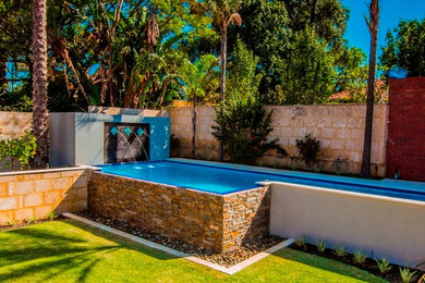 Large traditional backyard l-shaped infinity pool in Perth with a water feature and natural stone pavers.