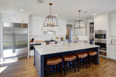 This is an example of a large transitional kitchen in Boston with a farmhouse sink, flat-panel cabinets, white cabinets, quartzite benchtops, white splashback, ceramic splashback, stainless steel appliances, medium hardwood floors and with island.