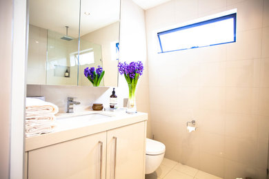 Photo of a contemporary bathroom in Melbourne with beige cabinets, an open shower, a wall-mount toilet, beige tile, ceramic tile, beige walls, ceramic floors, an undermount sink and solid surface benchtops.