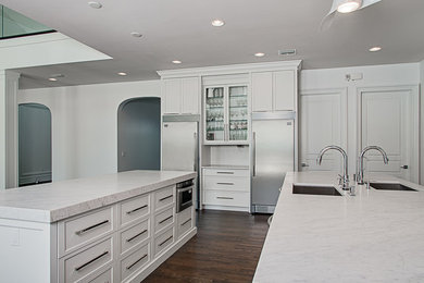 Open concept kitchen - large modern galley dark wood floor open concept kitchen idea in Tampa with an undermount sink, raised-panel cabinets, white cabinets, marble countertops, white backsplash, stone slab backsplash, stainless steel appliances and two islands