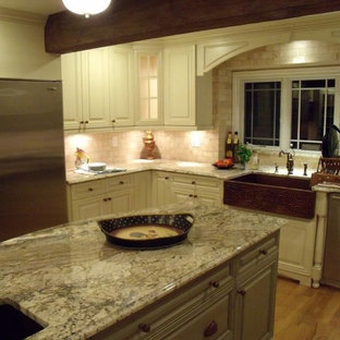 Cette image montre une arrière-cuisine traditionnelle en U de taille moyenne avec un évier de ferme, un placard avec porte à panneau surélevé, des portes de placard blanches, un plan de travail en granite, une crédence beige, une crédence en pierre calcaire, un électroménager en acier inoxydable, un sol en bois brun, un îlot central et un sol multicolore.
