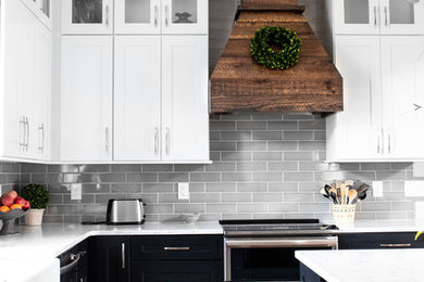 Mid-sized country l-shaped medium tone wood floor and brown floor eat-in kitchen photo in Charlotte with a farmhouse sink, shaker cabinets, black cabinets, quartz countertops, gray backsplash, subway tile backsplash, stainless steel appliances, an island and white countertops