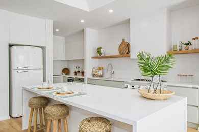This is an example of a beach style single-wall eat-in kitchen in Melbourne with an undermount sink, white splashback, stainless steel appliances, with island, white benchtop and vaulted.