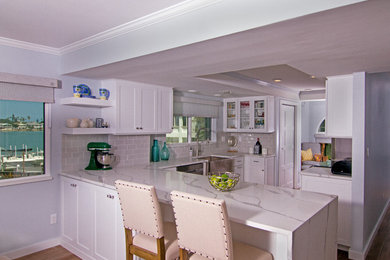 Example of a small l-shaped porcelain tile and brown floor open concept kitchen design in Tampa with a farmhouse sink, shaker cabinets, white cabinets, quartz countertops, gray backsplash, subway tile backsplash, stainless steel appliances and white countertops