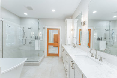 Example of a large transitional master white tile and porcelain tile porcelain tile, beige floor and double-sink bathroom design in Grand Rapids with shaker cabinets, white cabinets, a one-piece toilet, gray walls, an undermount sink, a hinged shower door, white countertops, a built-in vanity and quartz countertops