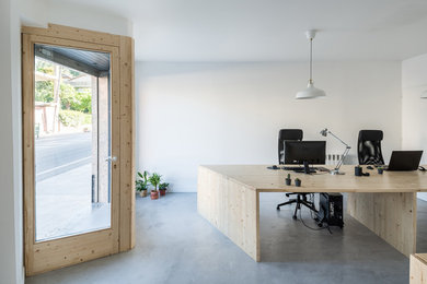 Ejemplo de estudio moderno de tamaño medio con paredes blancas, suelo de cemento, escritorio independiente y suelo gris