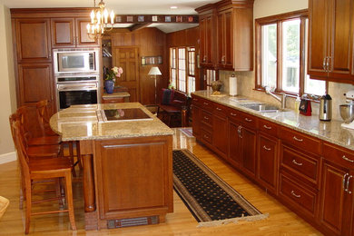Traditional eat-in kitchen in Boston with a farmhouse sink, raised-panel cabinets, medium wood cabinets, granite benchtops, stone tile splashback and panelled appliances.