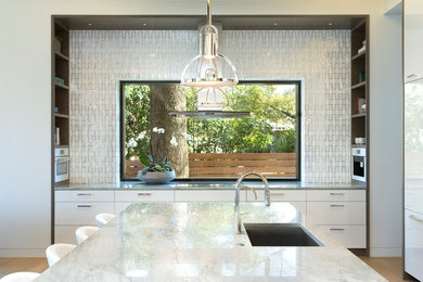 Kitchen - contemporary light wood floor and beige floor kitchen idea in Austin with an undermount sink, flat-panel cabinets, white cabinets, white appliances, an island and metallic backsplash