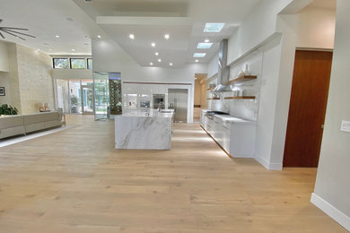 Inspiration for a large modern galley open plan kitchen in Sacramento with an undermount sink, flat-panel cabinets, white cabinets, quartz benchtops, white splashback, engineered quartz splashback, stainless steel appliances, light hardwood floors, with island, white benchtop and recessed.