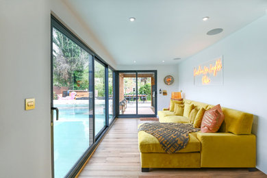 This is an example of a medium sized contemporary open plan living room in London with a home bar, white walls, light hardwood flooring, no fireplace and a wall mounted tv.