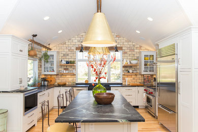Inspiration for a mid-sized country u-shaped eat-in kitchen in Other with a double-bowl sink, recessed-panel cabinets, white cabinets, granite benchtops, beige splashback, brick splashback, stainless steel appliances, light hardwood floors, with island and brown floor.