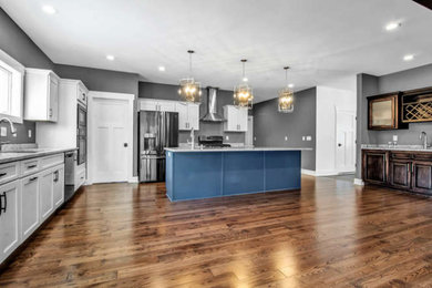 Example of a mid-sized transitional l-shaped medium tone wood floor and brown floor eat-in kitchen design in New York with an undermount sink, shaker cabinets, white cabinets, quartzite countertops, stainless steel appliances, an island and gray countertops