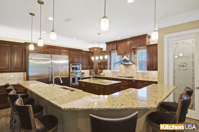 Inspiration for a large timeless l-shaped ceramic tile and brown floor eat-in kitchen remodel in Jacksonville with an undermount sink, raised-panel cabinets, brown cabinets, granite countertops, beige backsplash, subway tile backsplash, stainless steel appliances, two islands and brown countertops