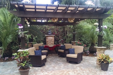 This is an example of a large tropical backyard patio in Miami with a water feature and natural stone pavers.