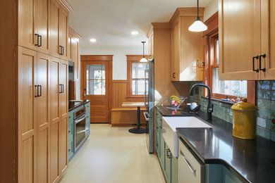 Example of a mid-sized transitional galley linoleum floor enclosed kitchen design in Portland with a farmhouse sink, shaker cabinets, light wood cabinets, quartzite countertops, blue backsplash, ceramic backsplash, stainless steel appliances and black countertops