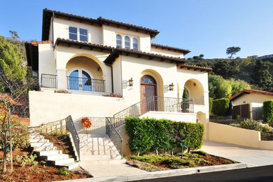 Inspiration for a large mediterranean beige two-story stucco house exterior remodel in Los Angeles with a hip roof and a tile roof