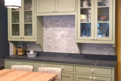 Example of a mid-sized arts and crafts l-shaped medium tone wood floor enclosed kitchen design in New York with a farmhouse sink, shaker cabinets, green cabinets, soapstone countertops, gray backsplash, stone tile backsplash, stainless steel appliances and an island