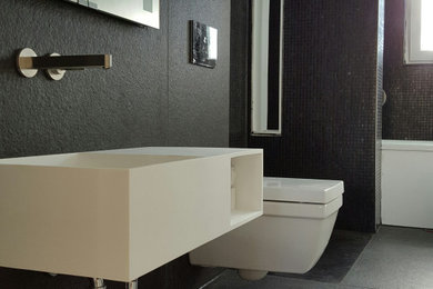 Mittelgroßes Modernes Badezimmer mit Badewanne in Nische, bodengleicher Dusche, Wandtoilette, schwarzen Fliesen, Steinfliesen, schwarzer Wandfarbe, Wandwaschbecken, Mineralwerkstoff-Waschtisch, schwarzem Boden und Falttür-Duschabtrennung in Hannover