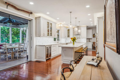 Photo of a mid-sized transitional u-shaped eat-in kitchen in DC Metro with an undermount sink, recessed-panel cabinets, white cabinets, quartz benchtops, white splashback, ceramic splashback, stainless steel appliances, medium hardwood floors, with island, brown floor and white benchtop.