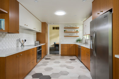 Photo of a mid-sized midcentury u-shaped eat-in kitchen in Los Angeles with an undermount sink, flat-panel cabinets, medium wood cabinets, quartz benchtops, white splashback, ceramic splashback, stainless steel appliances, porcelain floors, grey floor and white benchtop.