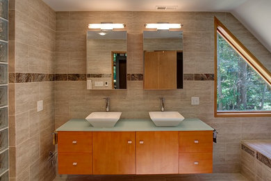 Inspiration for a mid-sized modern master bathroom in Baltimore with flat-panel cabinets, medium wood cabinets, a drop-in tub, beige tile, porcelain tile, beige walls, limestone floors, a vessel sink and glass benchtops.