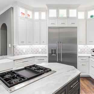 Klassisk inredning av ett stort grå grått kök, med en rustik diskho, luckor med upphöjd panel, grå skåp, bänkskiva i kvartsit, grått stänkskydd, stänkskydd i kalk, rostfria vitvaror, mörkt trägolv, en halv köksö och brunt golv