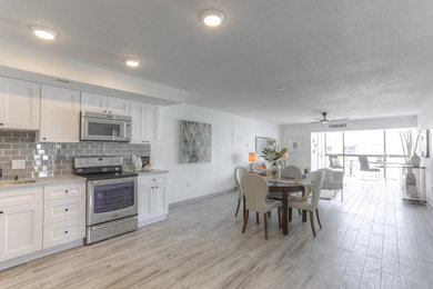 Photo of a large transitional l-shaped eat-in kitchen in Tampa with a single-bowl sink, shaker cabinets, white cabinets, quartz benchtops, grey splashback, glass tile splashback, stainless steel appliances, porcelain floors and no island.