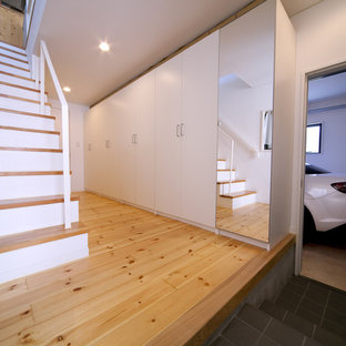 На фото: маленькие узкие прихожие в стиле модернизм с белыми стенами, полом из фанеры, одностворчатой входной дверью, черной входной дверью и бежевым полом