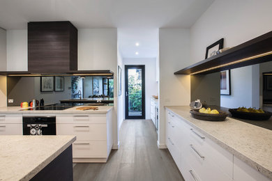 This is an example of a contemporary l-shaped open plan kitchen in Melbourne with an undermount sink, white cabinets, quartz benchtops, mirror splashback, light hardwood floors, with island and flat-panel cabinets.