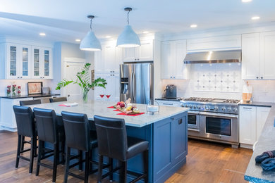 Open concept kitchen - large transitional l-shaped medium tone wood floor and brown floor open concept kitchen idea in Philadelphia with recessed-panel cabinets, white cabinets, granite countertops, white backsplash, porcelain backsplash, stainless steel appliances, an island and gray countertops